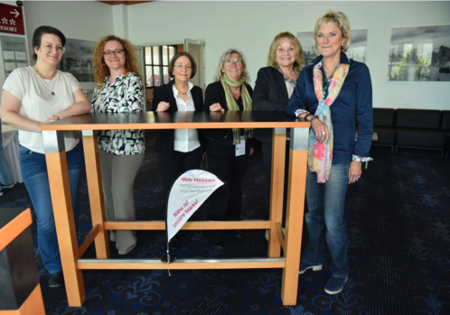 Sechs Frauen stehen an einem Stehtisch und blicken in die Kamera. 