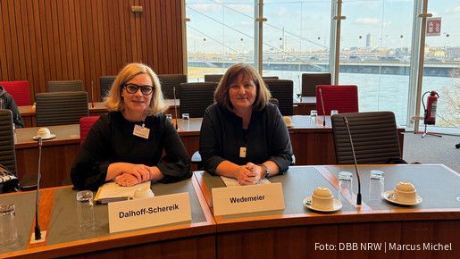 Zwei Frauen sitzen an einem Tisch in einem Plenarsaal