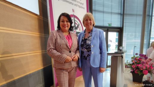 Zwei Frauen stehen auf einer Bühne und schauen in die Kamera